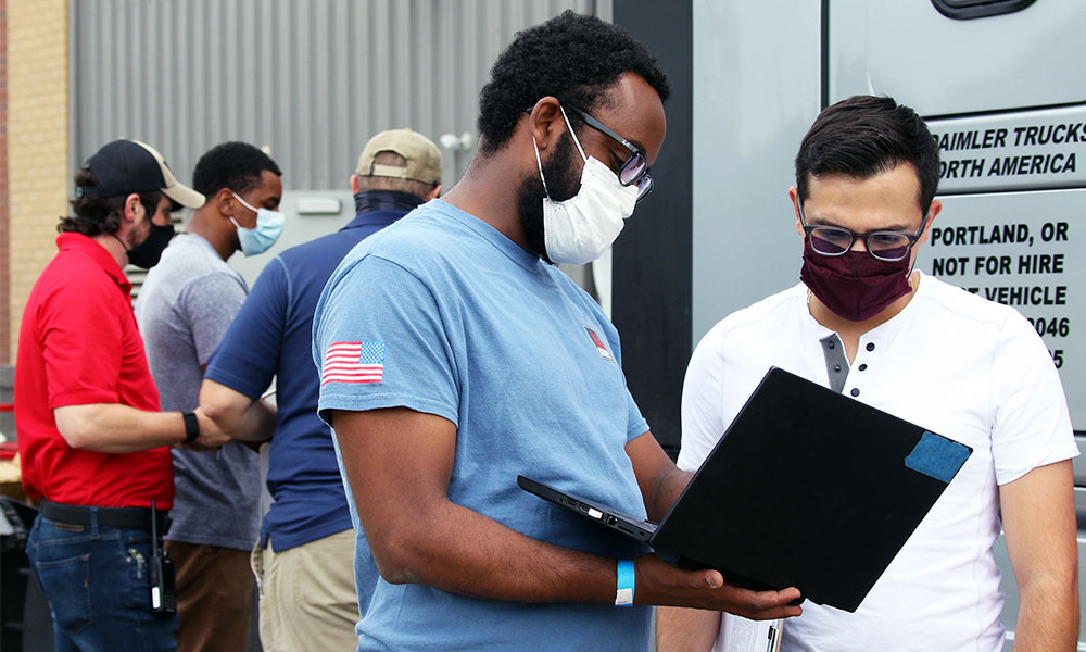 two employees wearing masks looking at a laptop