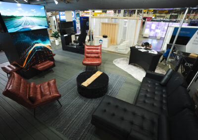 The inside of Torc Robotics' booth at Manifest 2025. Several black couches and brown leather loveseats surround a coffee table; TVs mounted on the walls offer a look at the Torc truck on the road.