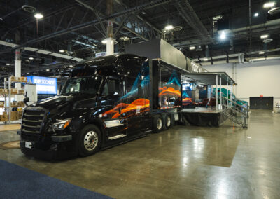 Torc Robotics' booth at Manifest 2025: a black semi-truck wherein the trailer is broken out into a place to sit, learn more about Torc, and talk to the Torc team