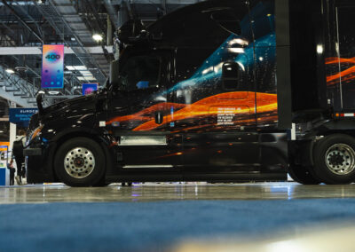 Torc's autonomous truck at Manifest 2025; a black semi-truck, wrapped with orange and blue abstract shapes, parked beneath a Torc sign